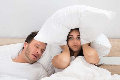 Woman holding pillow over her head while man sleeps next to her, centerville oh