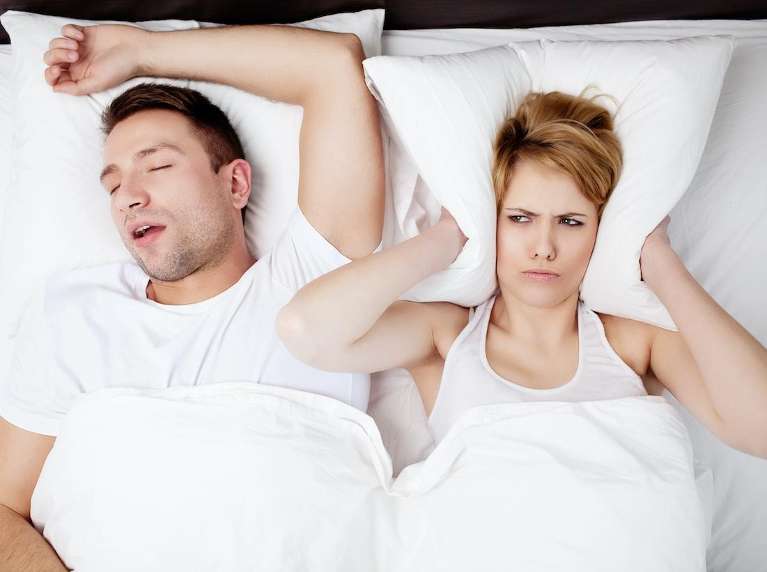 Woman with pillow covering ears next to man snoring in bend, centerville oh