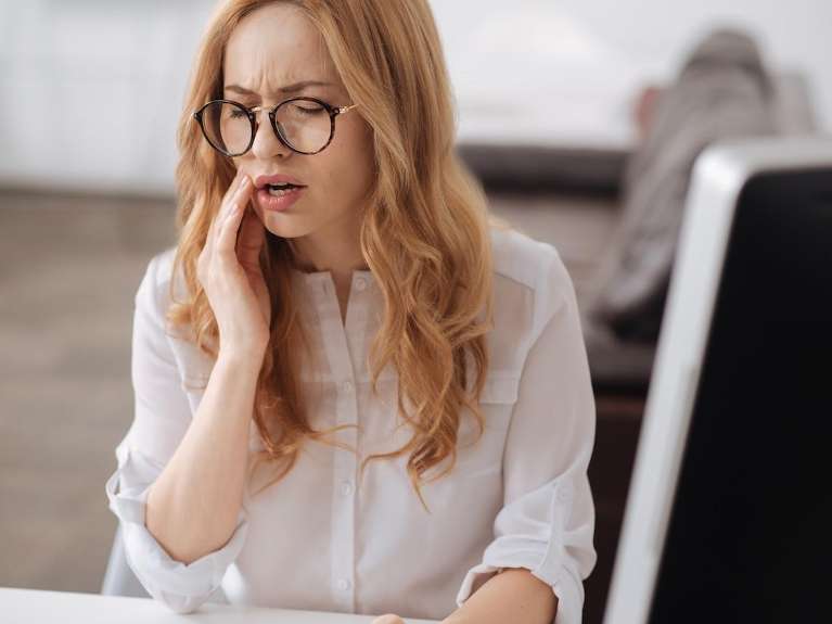 Woman with red hair and glasses holding her jaw in pain, centerville oh